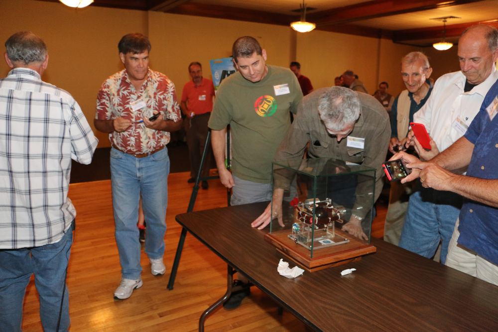 Conference attendees gathered around a device in a glass case on a demonstration table at ESTC 2015